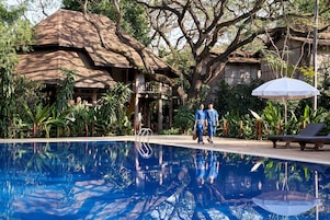 Uma área de piscina com uma estrutura de telhado de palha, uma espreguiçadeira e um guarda-sol suspenso.