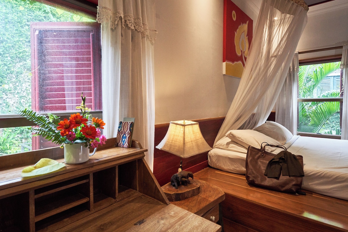 Una habitación con cama, mesita de noche, lámpara y ventana con cortinas.