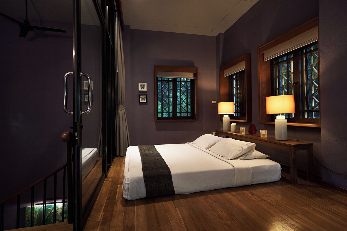 Un dormitorio con una cama grande, piso de madera, ventana con vistas y puerta con panel de vidrio.