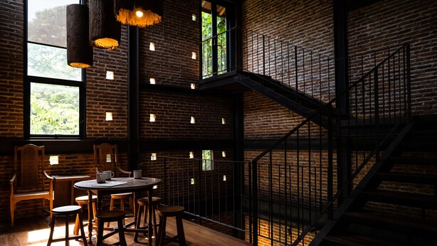 A modern interior with exposed brick walls, a wooden dining area, and a staircase. - Kaomai Lanna Resort (San Pa Thong)