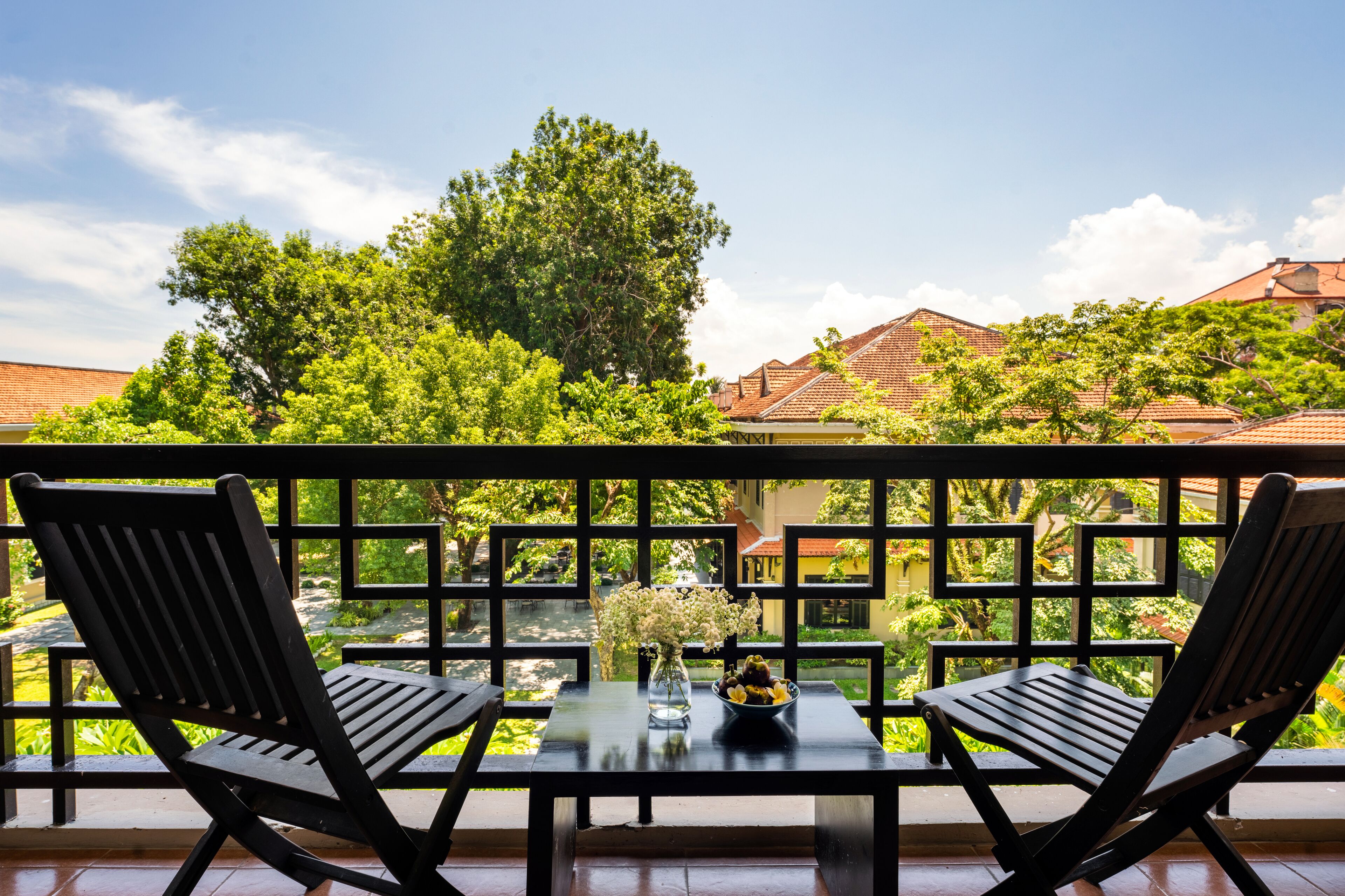 A balcony with two wooden chairs, a glass table, and a vase of flowers.