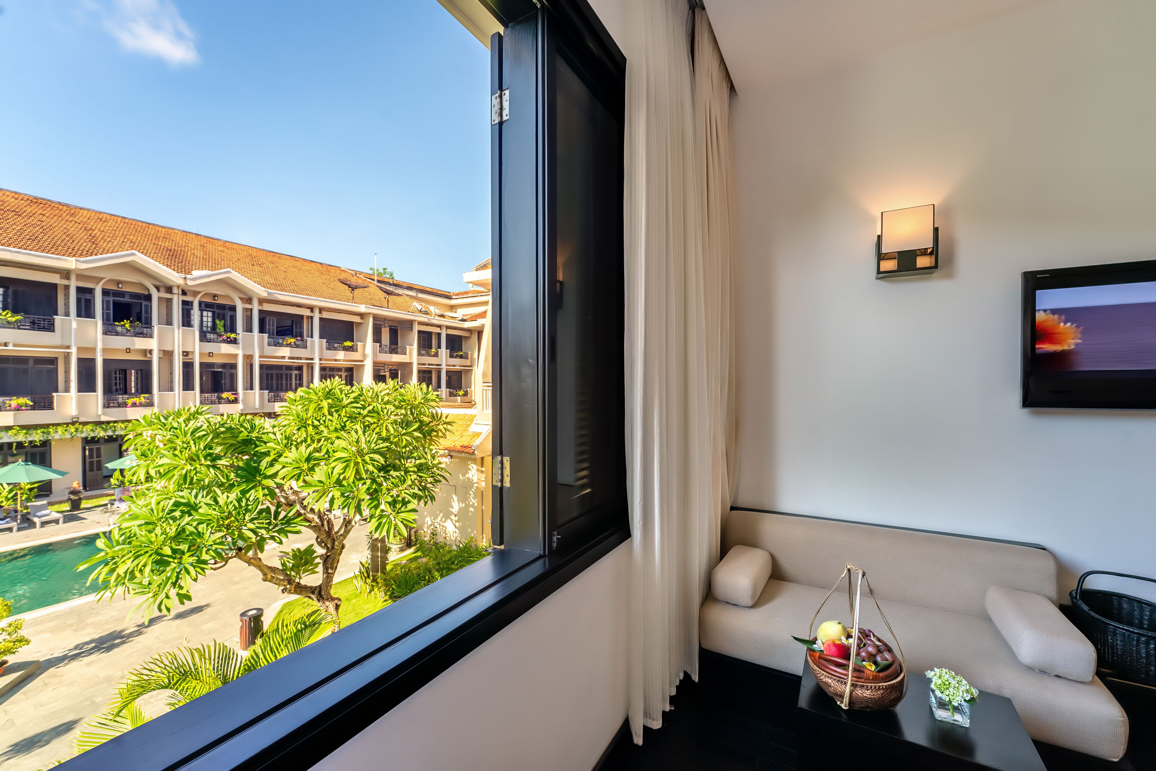 A hotel room with a balcony, a sofa, a small table, and a view of a pool and building.