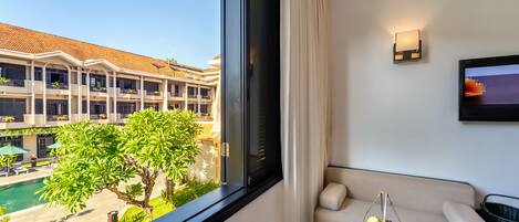 A hotel room with a balcony, a sofa, a small table, and a view of a pool and building.