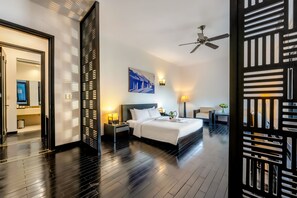 Una habitación de hotel moderna con una cama grande, un ventilador de techo, una mesita de noche con lámpara y un cuadro colgado en la pared.