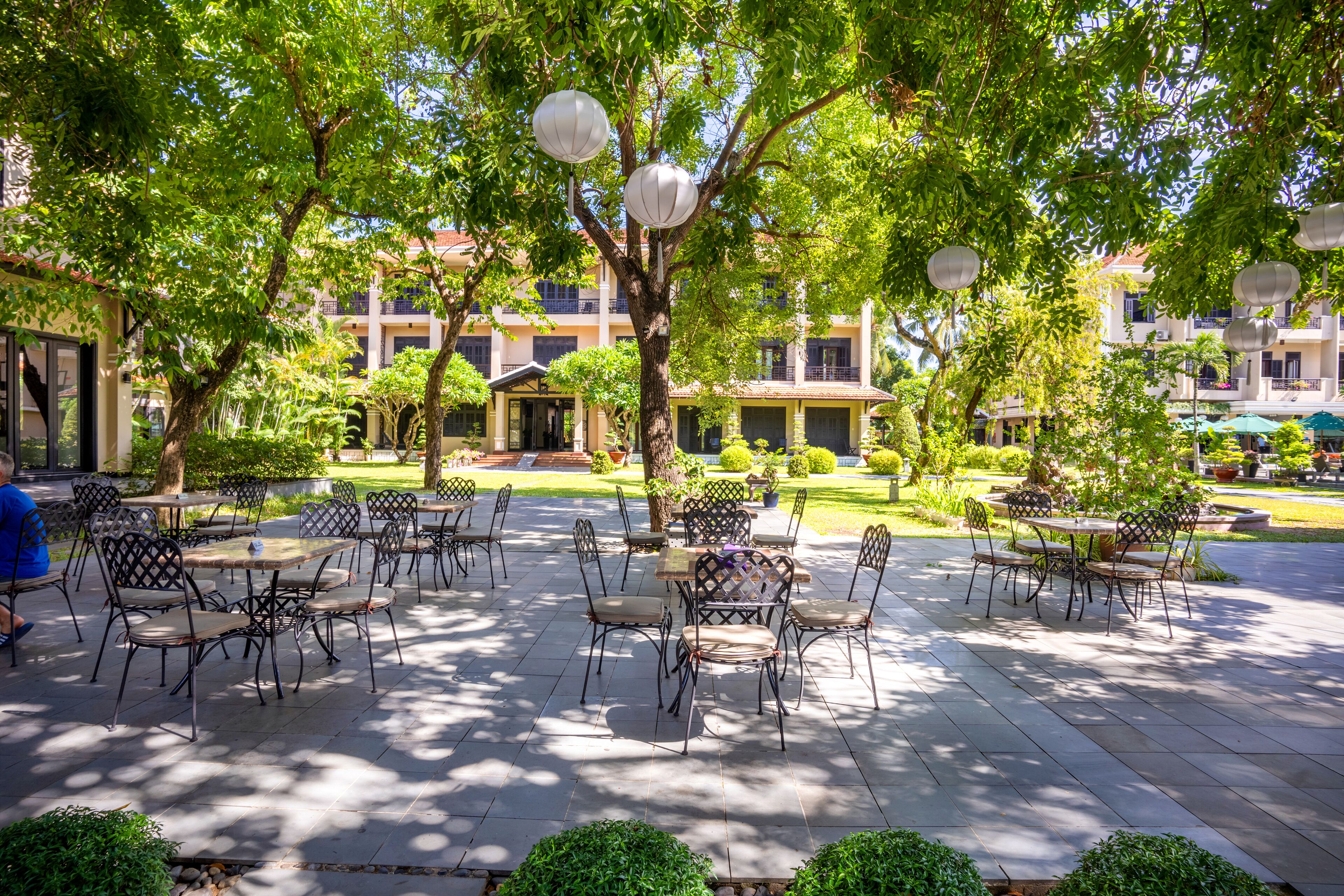 An outdoor patio area with tables and chairs, surrounded by trees and buildings.