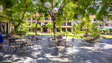 An outdoor patio area with tables and chairs, surrounded by trees and buildings.