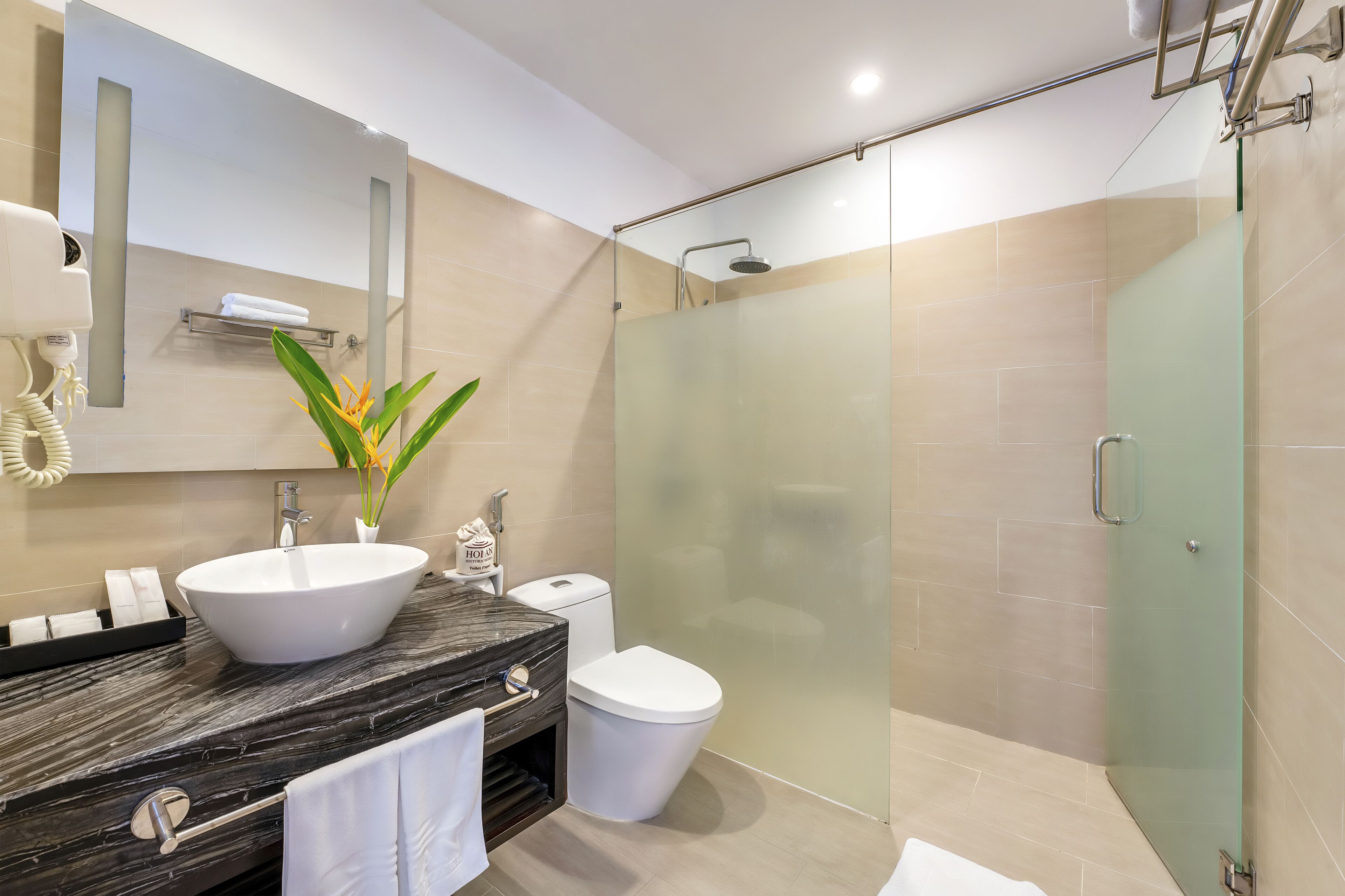A modern bathroom with a marble vanity, a white sink, a glass-enclosed shower, and a toilet.
