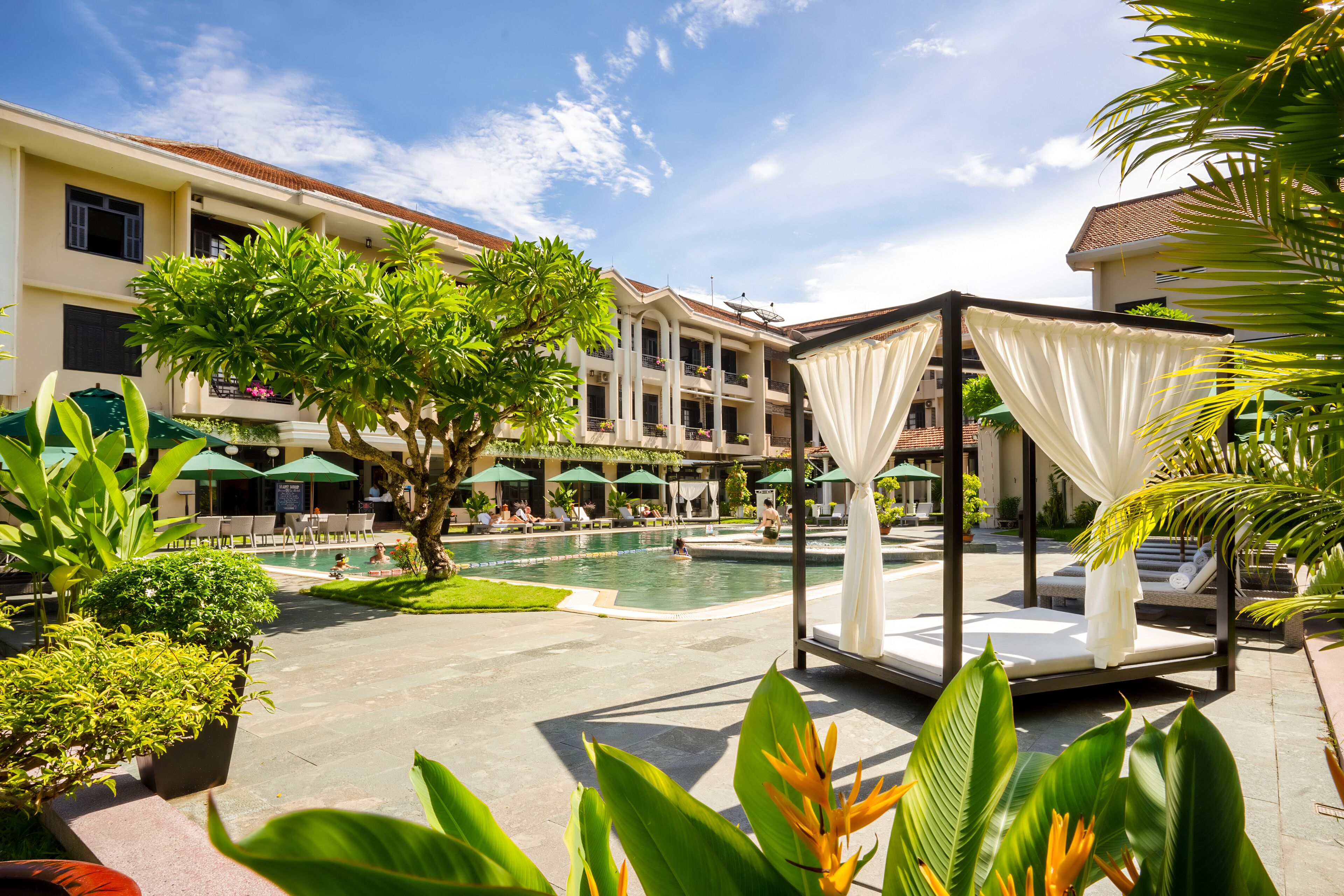 A resort pool area with a cabana, lounge chairs, and a large building with balconies.