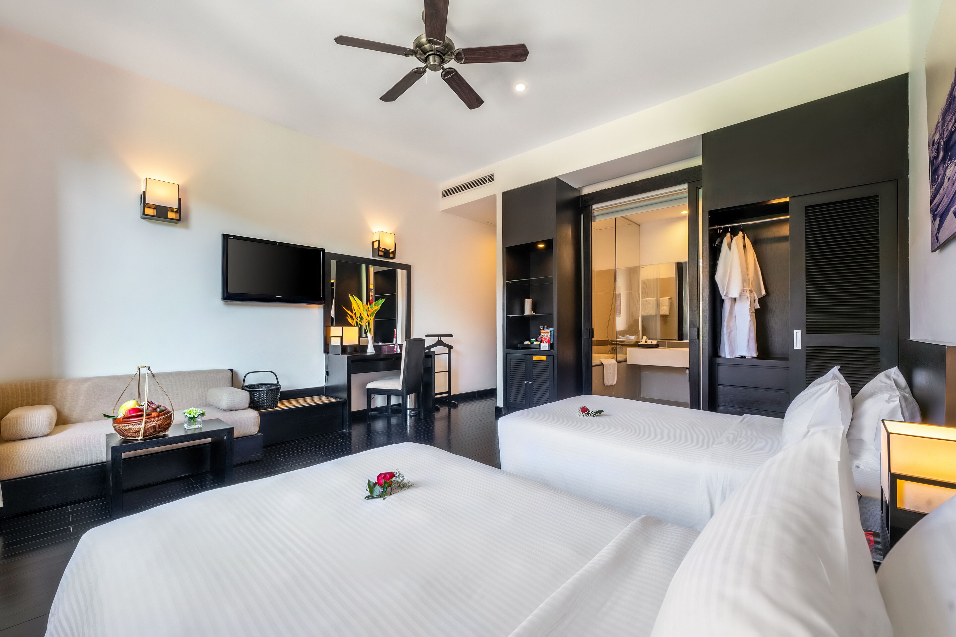 A hotel room with two beds, a sofa, a desk, a TV, and a bathroom visible through an open door.