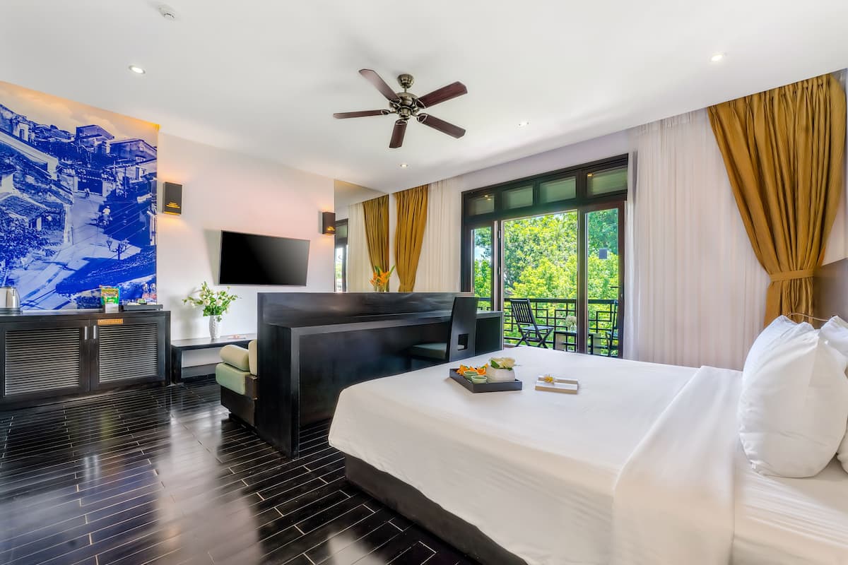 A modern hotel room with a large bed, a flat-screen TV, a ceiling fan, and a balcony with curtains.