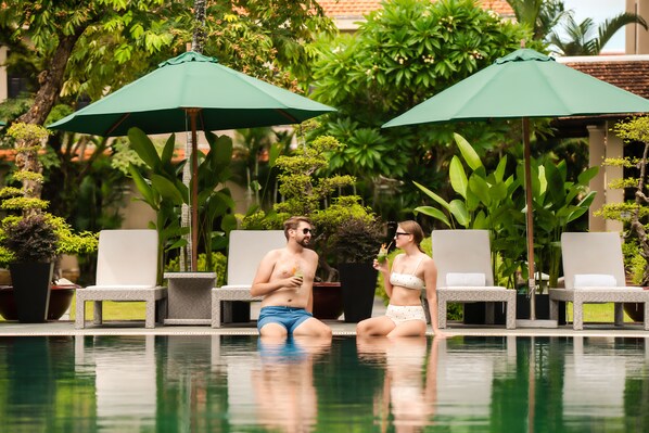 A poolside area with lounge chairs and umbrellas, surrounded by lush greenery. - Hoi An Historic Hotel (Da Nang)