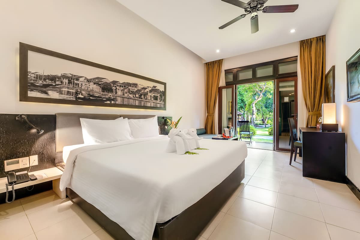 A hotel room with a large bed, a desk, a phone, a ceiling fan, and a view of the outdoors.