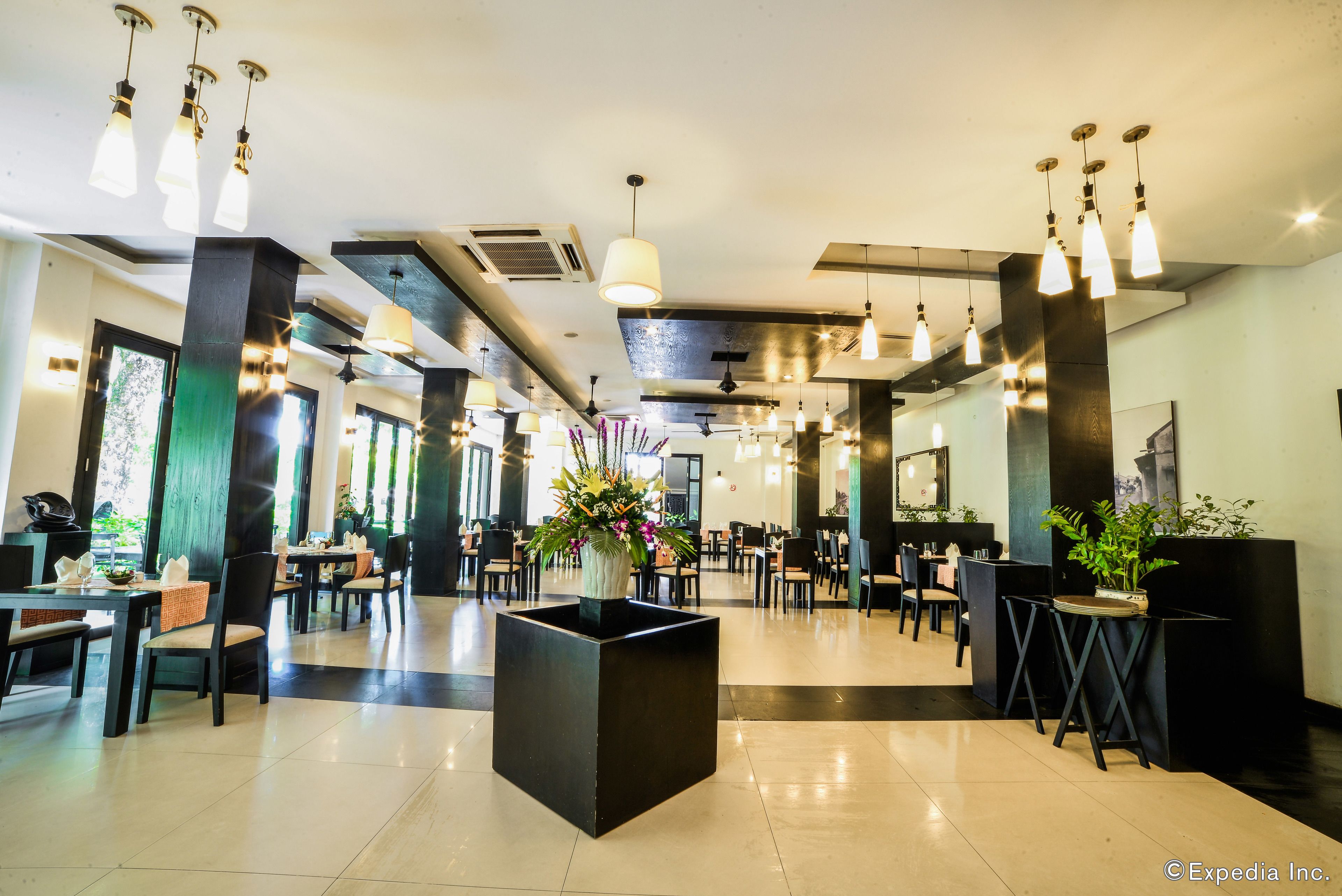 A spacious hotel lobby with modern decor, including black and white furniture, hanging pendant lights, and potted plants.