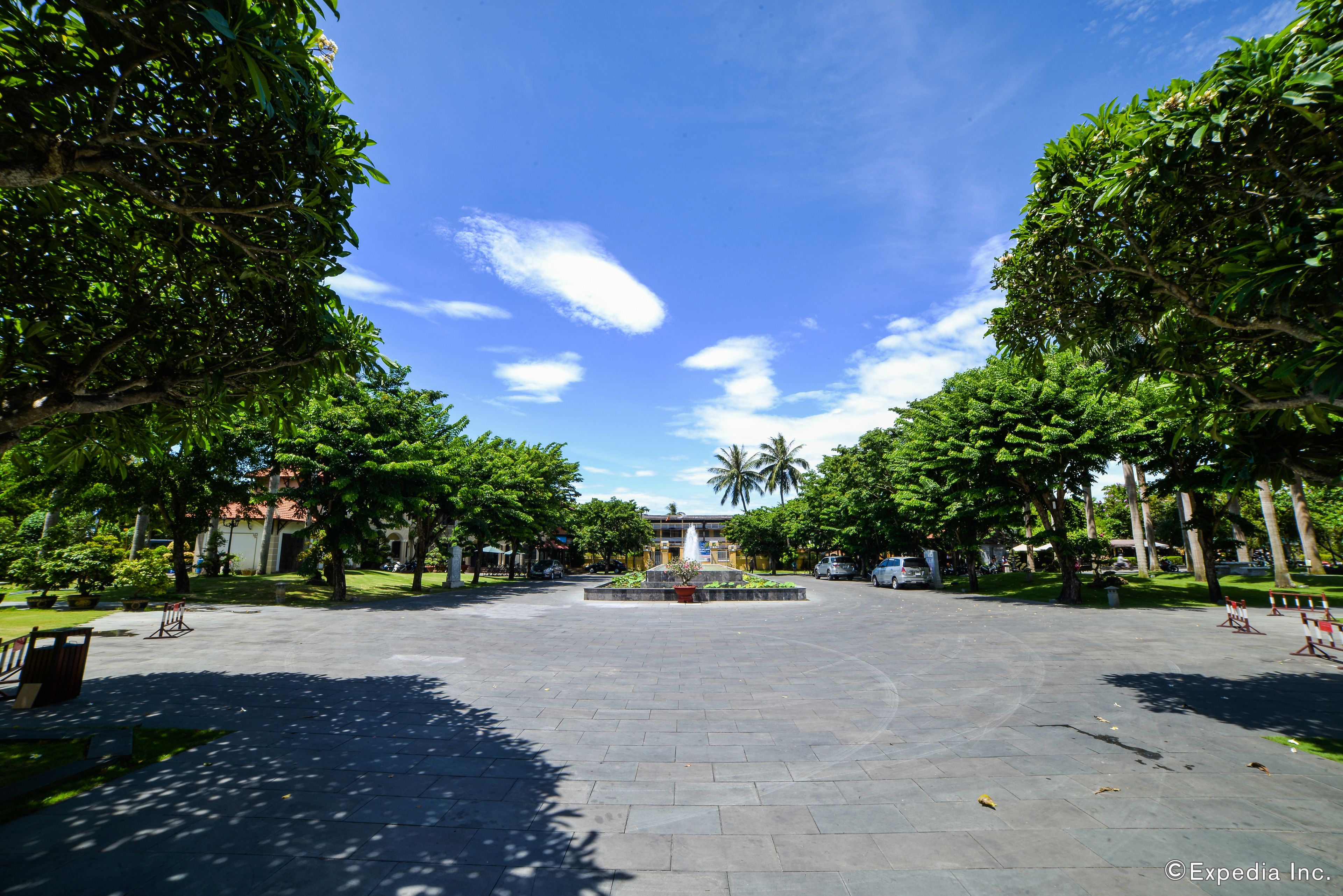 A spacious courtyard with a central fountain, surrounded by lush green trees and a clear blue sky.