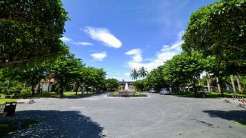 A spacious courtyard with a central fountain, surrounded by lush green trees and a clear blue sky.
