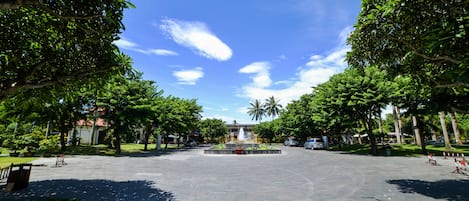A spacious courtyard with a central fountain, surrounded by lush green trees and a clear blue sky.