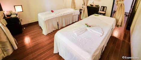 Une chambre d’hôtel avec deux lits, une petite table avec une lampe, un miroir et un tableau représentant des fleurs accroché au mur.