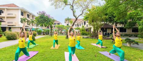 A group of people performing yoga on mats in an outdoor setting with buildings in the background.