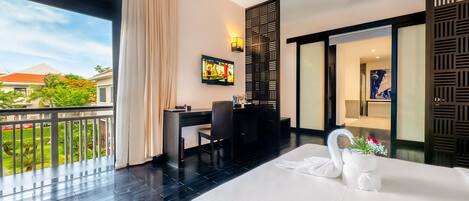 Una habitación de hotel con balcón, escritorio, cama decorada con cisne y televisor montado en la pared.