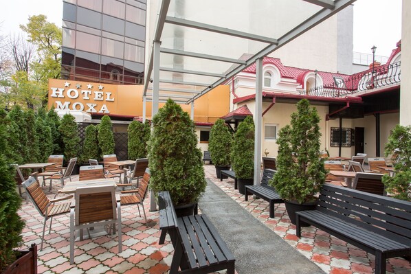 Un patio de hotel con mobiliario exterior, árboles en macetas y un edificio con un cartel.