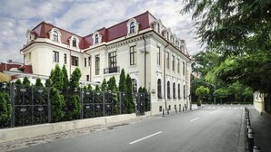 Un edifici gran i històric amb teulada vermella i parets blanques, envoltat per una tanca alta i arbres.