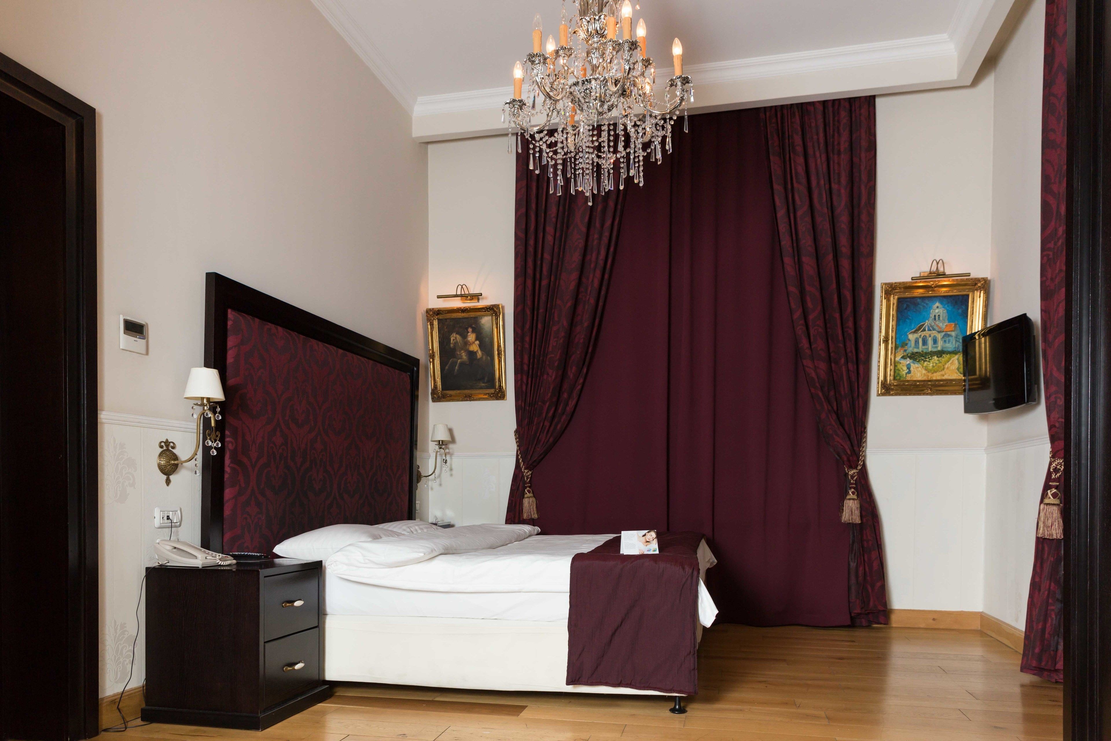 Une chambre à coucher avec un grand lit, un lustre, une table de chevet, un téléphone et un tableau au mur.