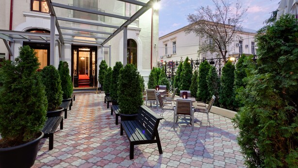 Un pati amb una teulada de vidre, bancs, arbres en testos i mobiliari per a l'exterior.