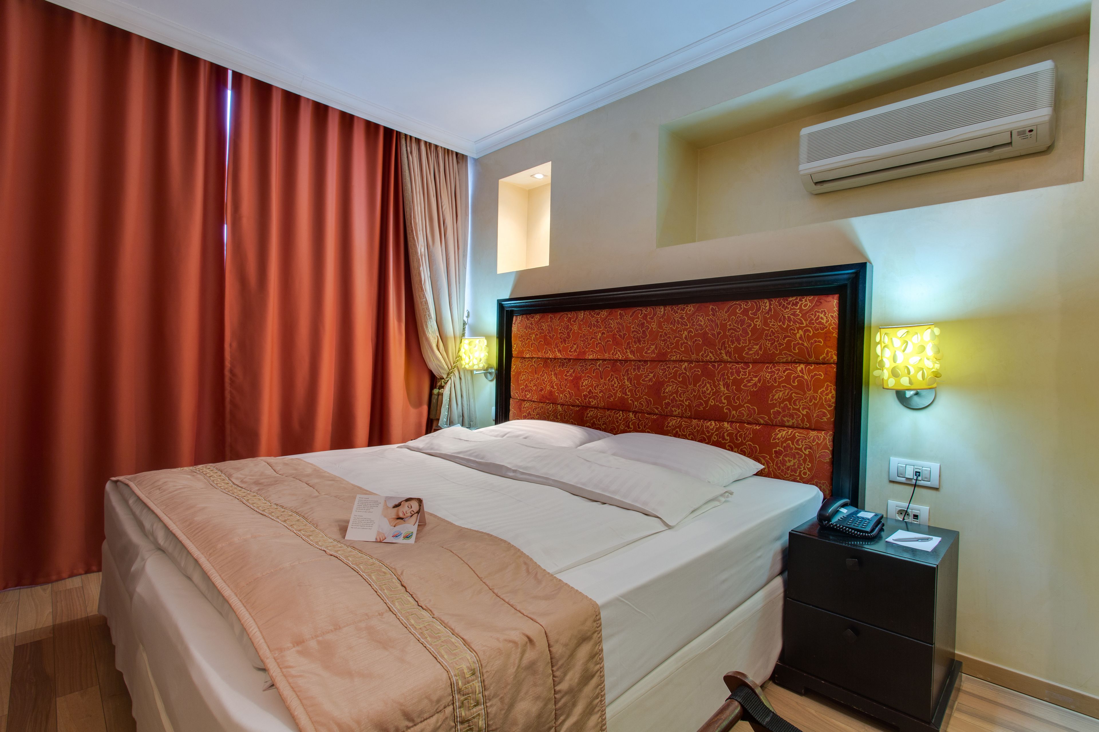 A hotel room with a bed, nightstand, and a wall-mounted air conditioner.