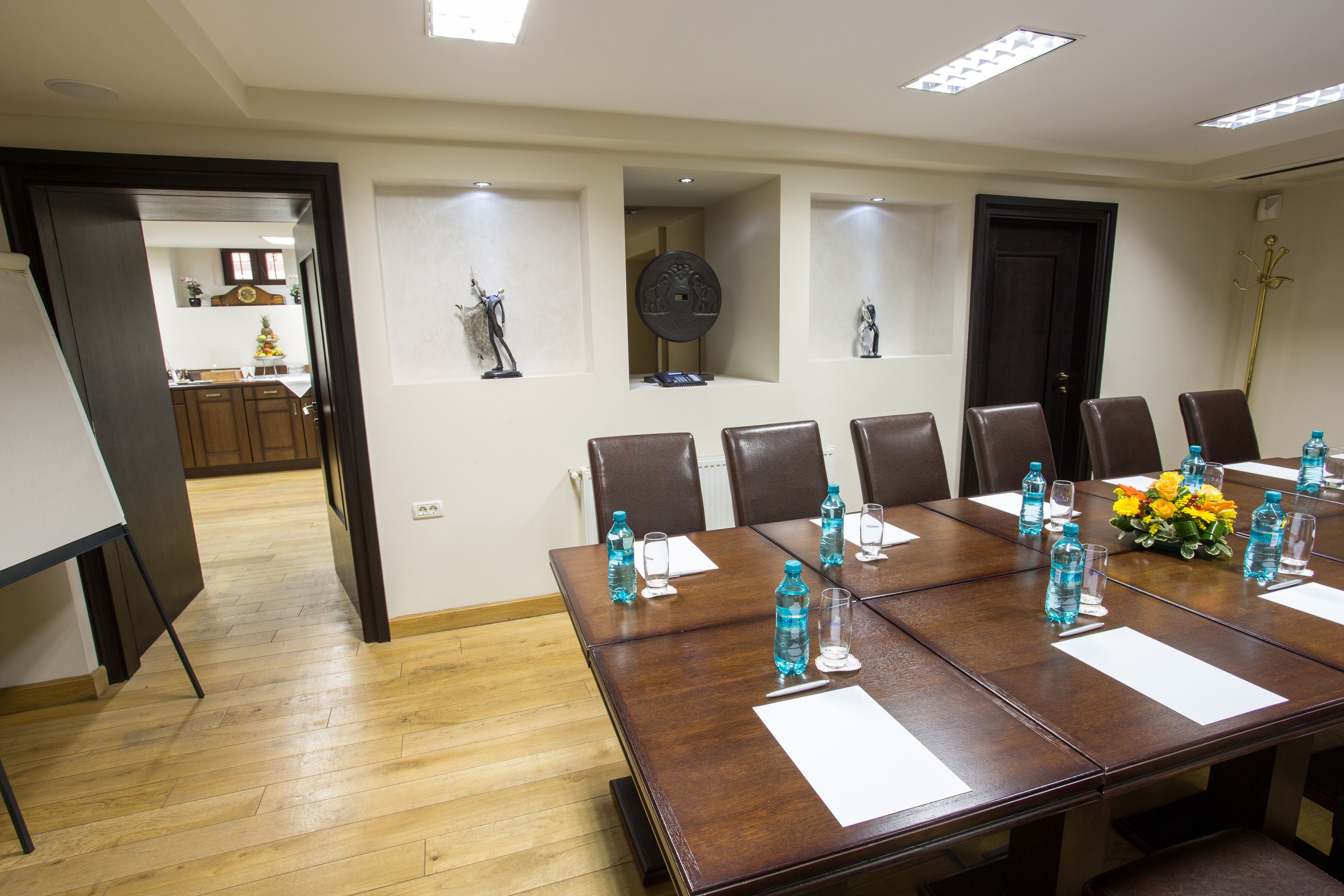 A conference room with a long table, chairs, water bottles, and a vase of flowers.