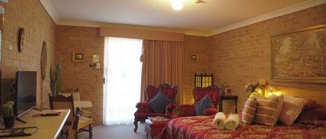 Habitación de hotel con pared de ladrillo, una cama grande con ropa de cama roja, dos sillones, una mesita y un televisor.