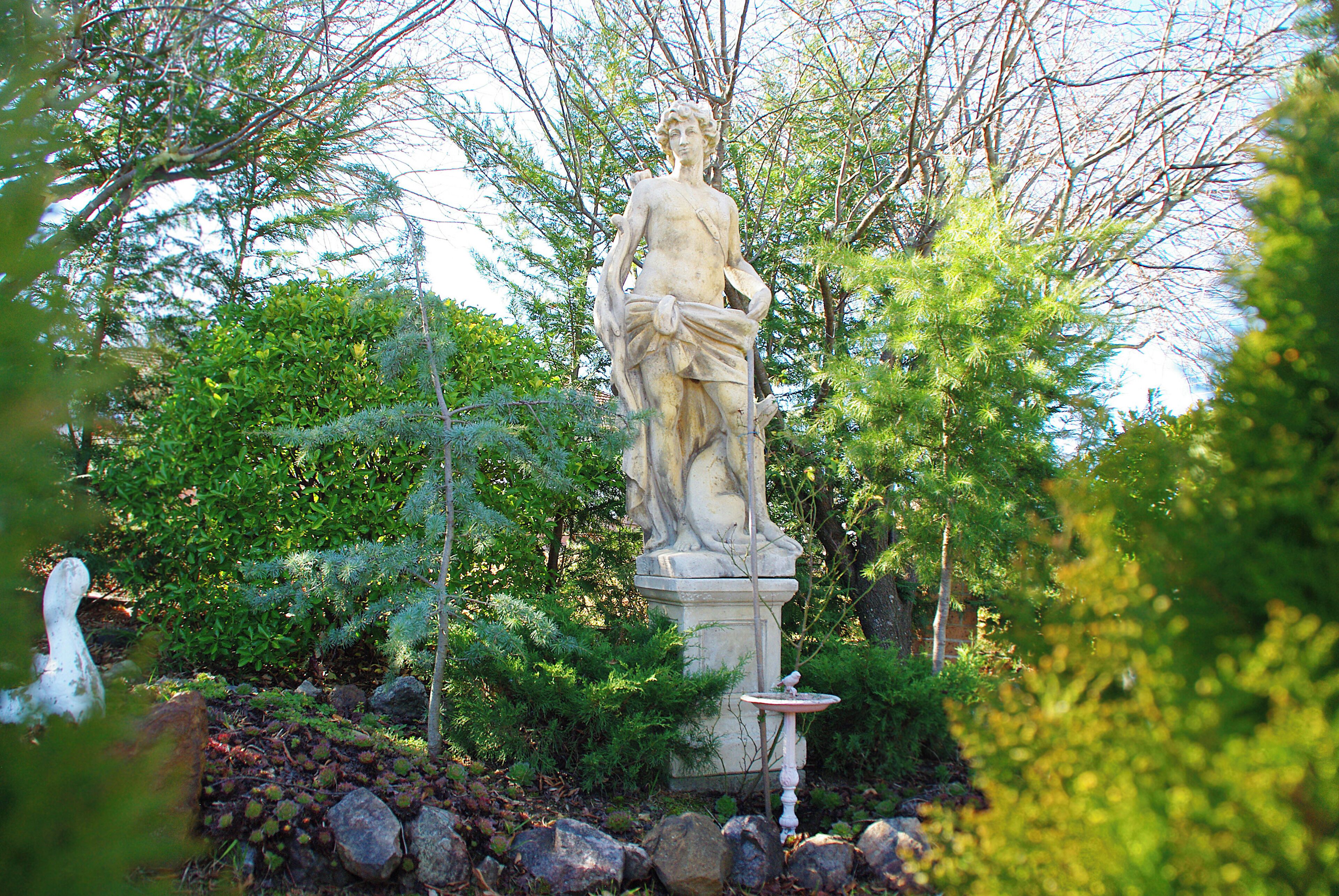 A statue in a garden with trees and rocks.