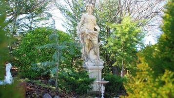 A statue in a garden with trees and rocks.