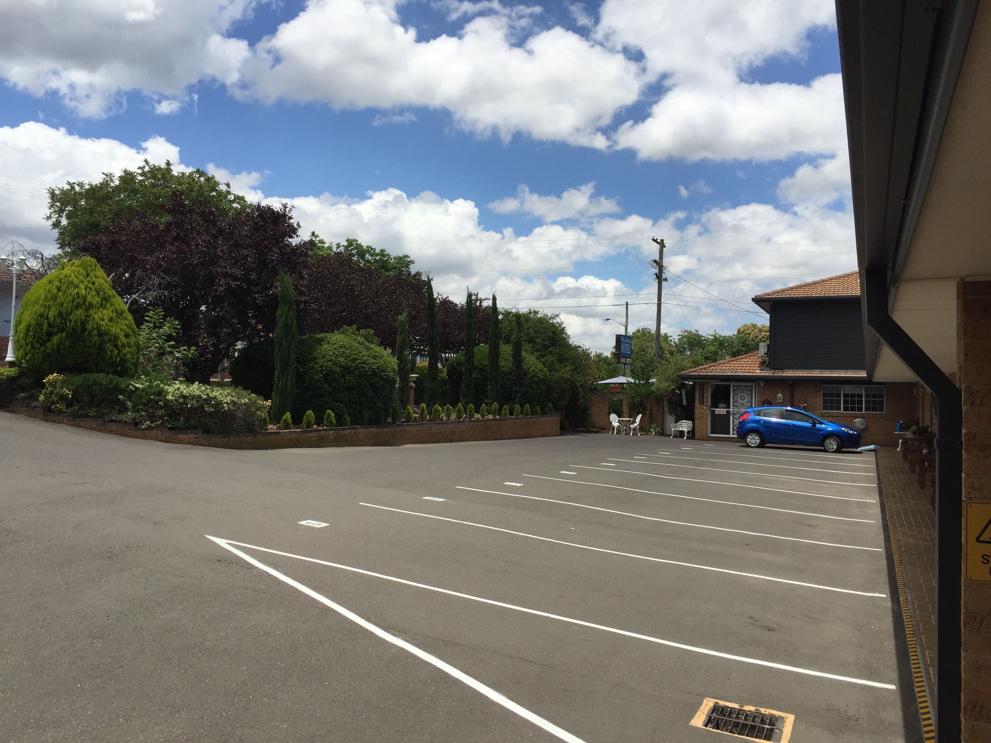 A parking lot with marked spaces, a blue car, and a building with a tiled roof.