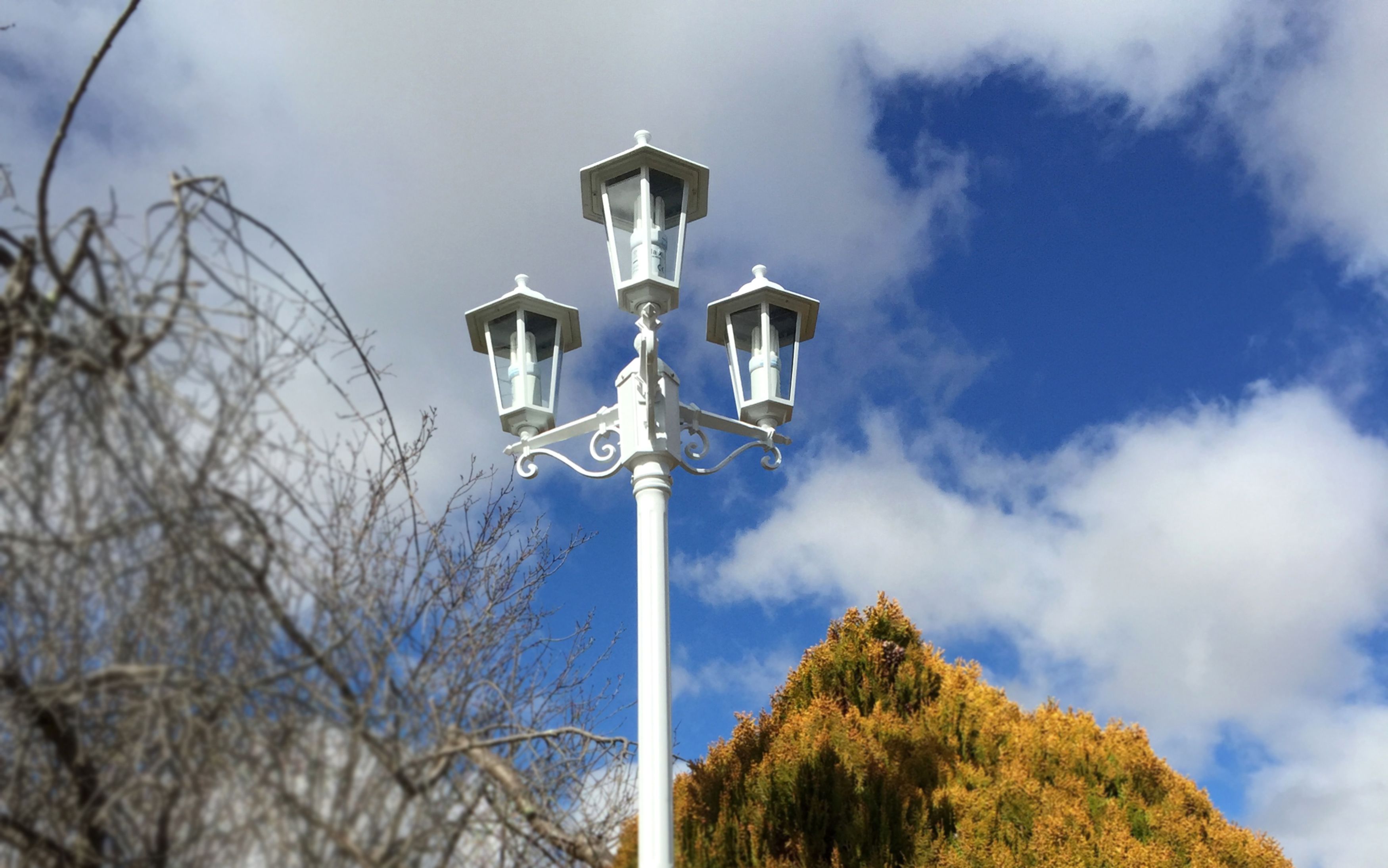 Lampione bianco con tre luci su uno cielo azzurro con nuvole.