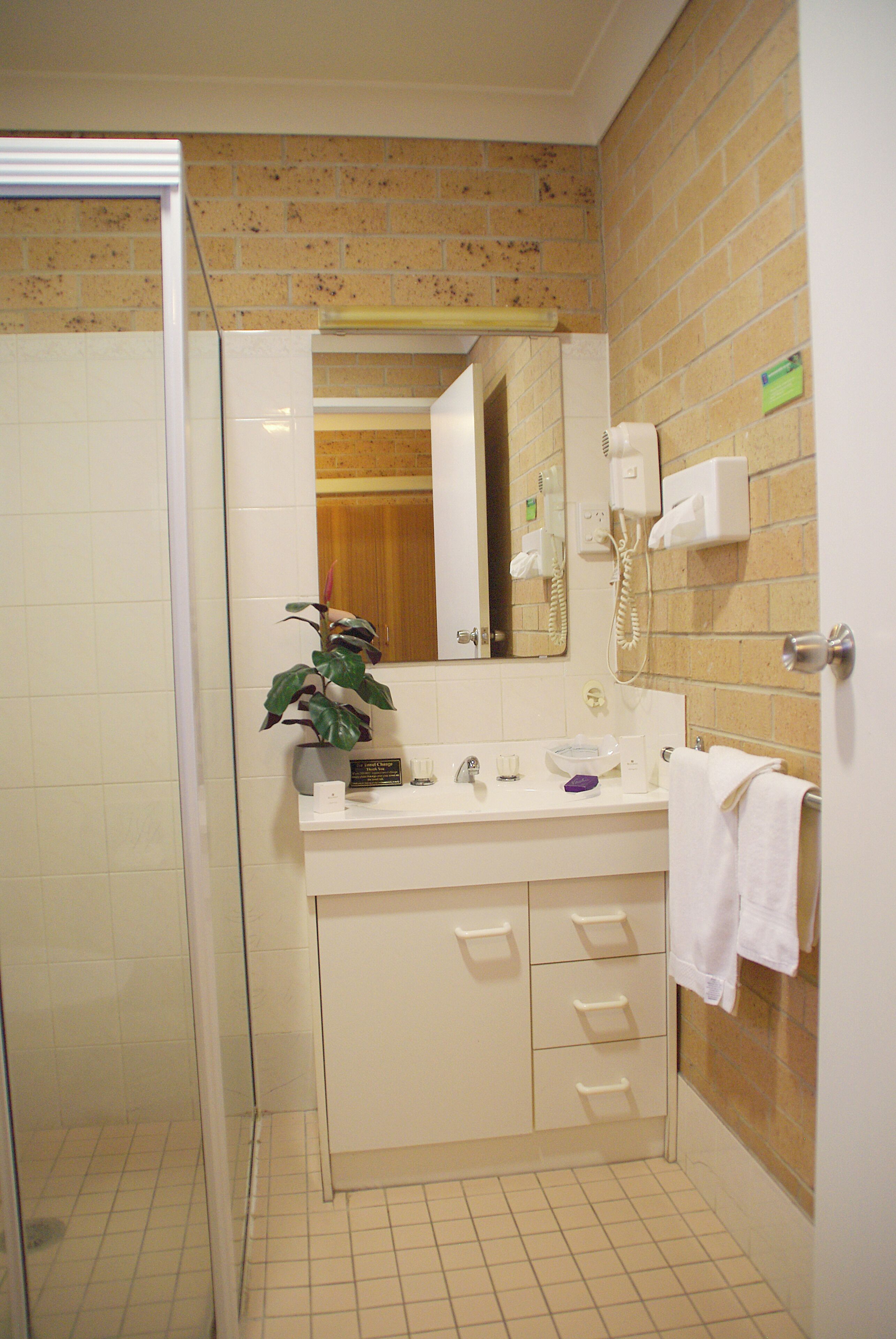 Ein Badezimmer mit Dusche, Waschbecken mit Spiegel, Fön und Handtuchhalter.
