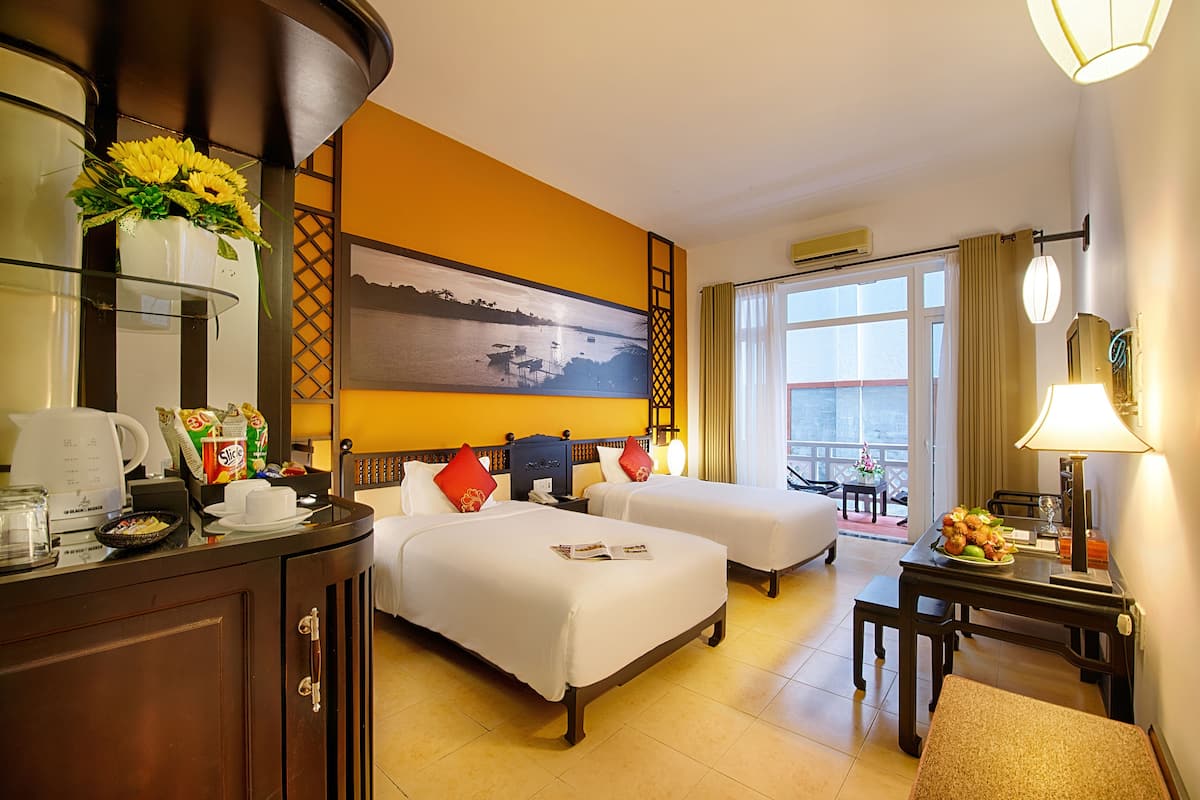 A hotel room with two beds, a desk, a coffee maker, a dining table with a plate of food, and a large window with a view.