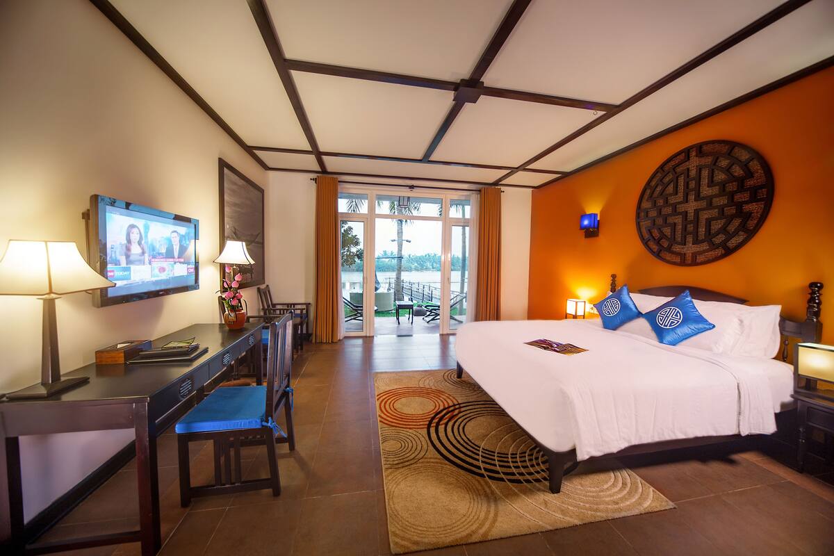 A hotel room with a bed, desk, chair, TV, and a view of the outdoors.
