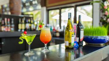 Two cocktails on a bar counter with bottles and a bowl in the background.