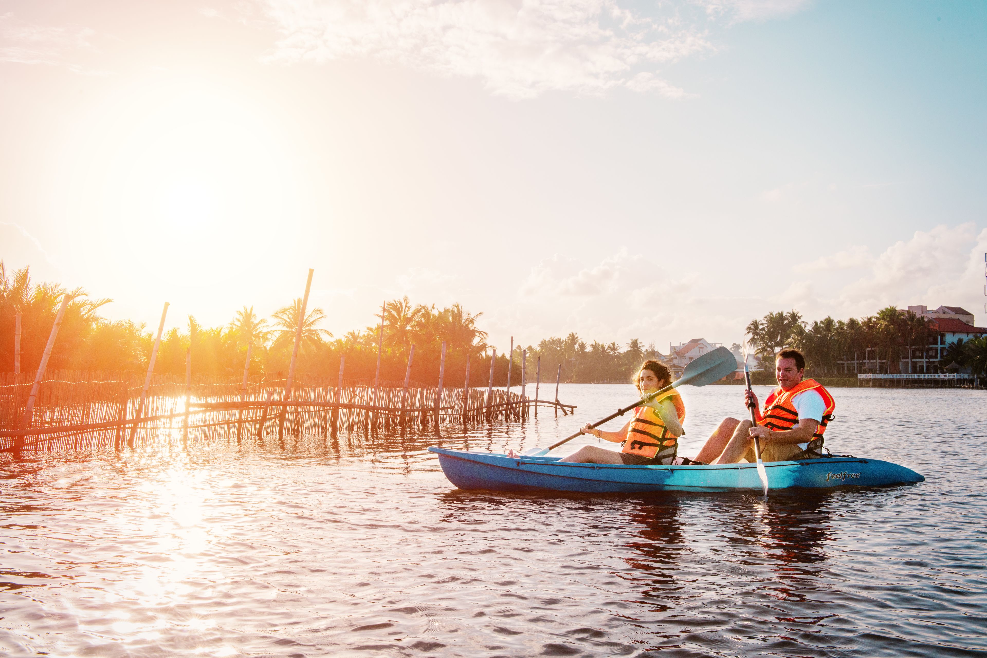 Two people in a blue kayak on calm water, wearing life jackets.