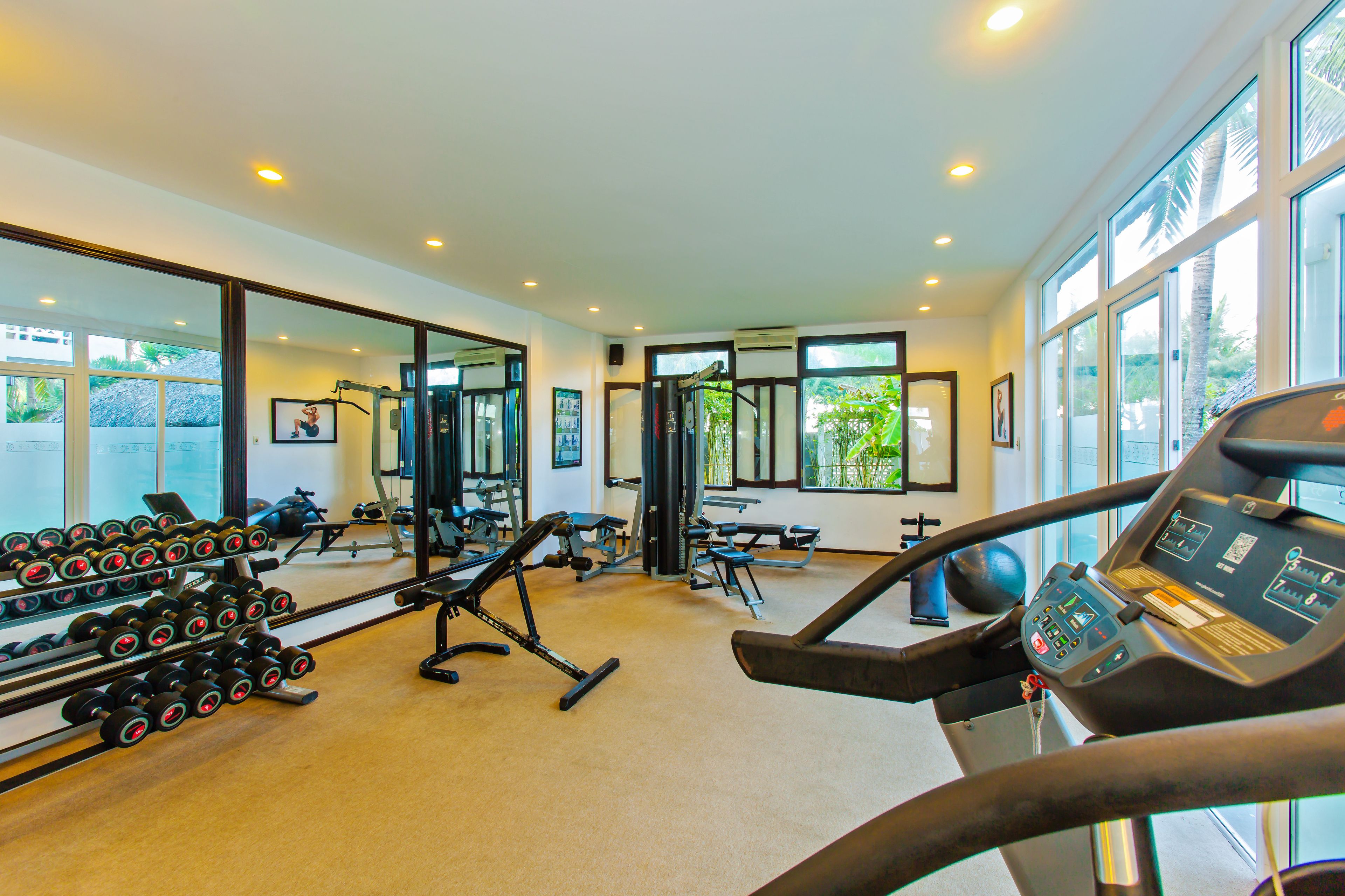 Un gimnasio con equipamiento de ejercicio, ventanas amplias y una cinta de correr.