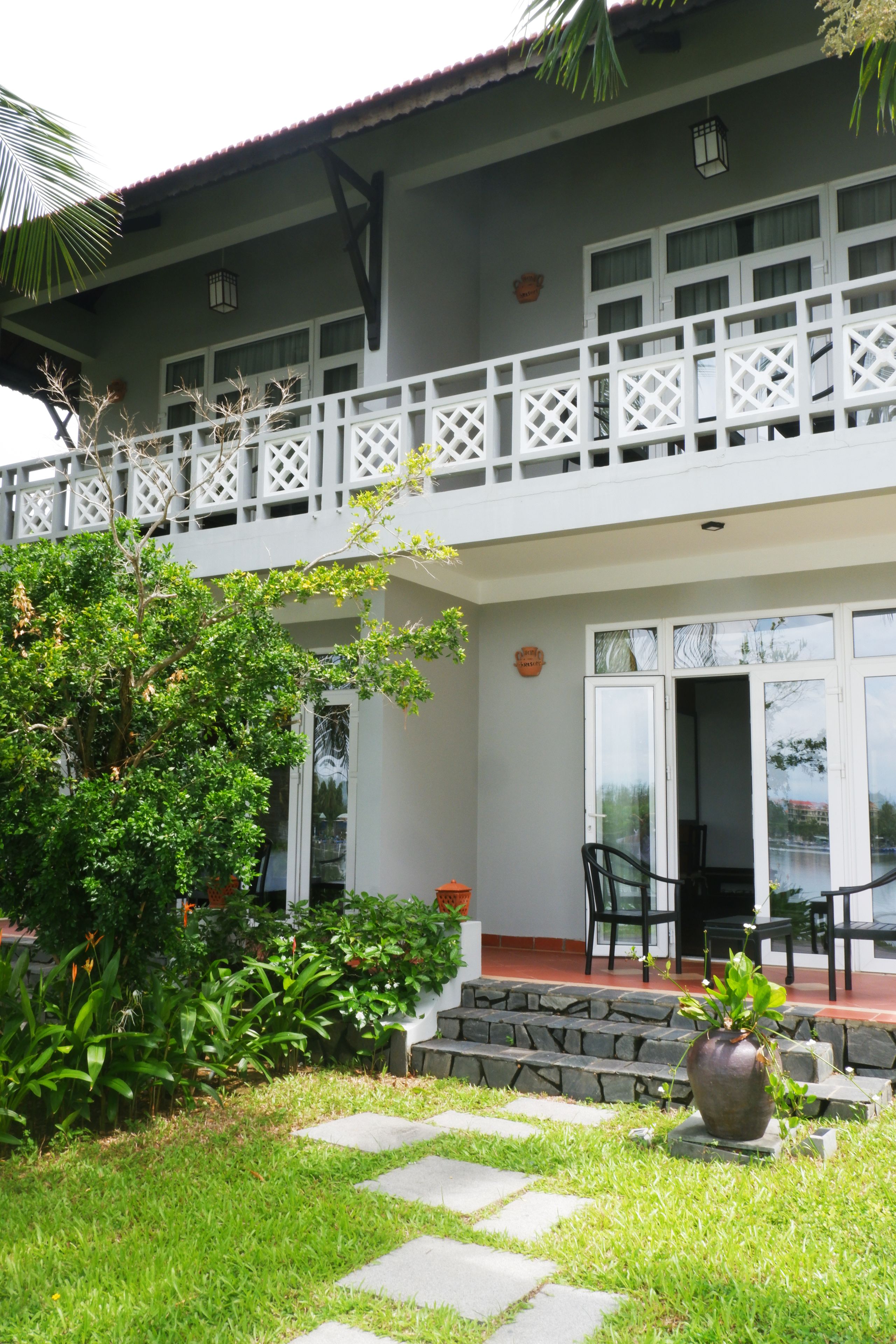 A two-story building with a balcony, a garden with a pathway, and a large potted plant.