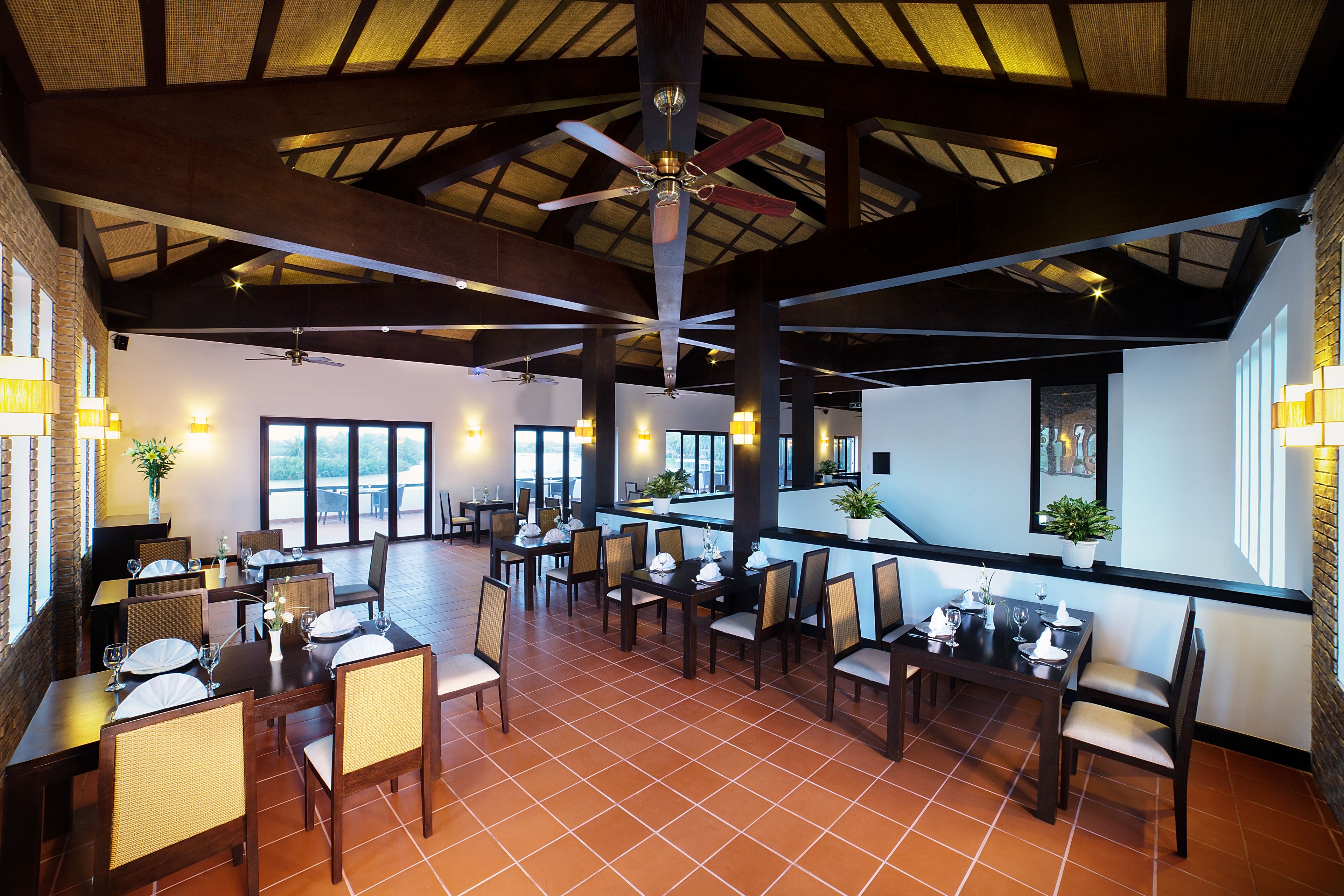 A spacious dining area with multiple tables and chairs, a ceiling fan, and large windows allowing natural light.
