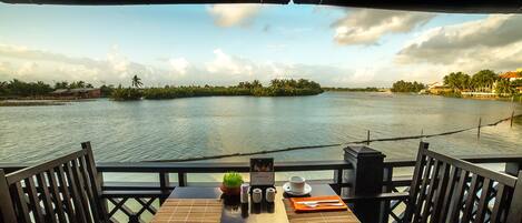 A table set for two with a view of a calm river and distant palm trees.
