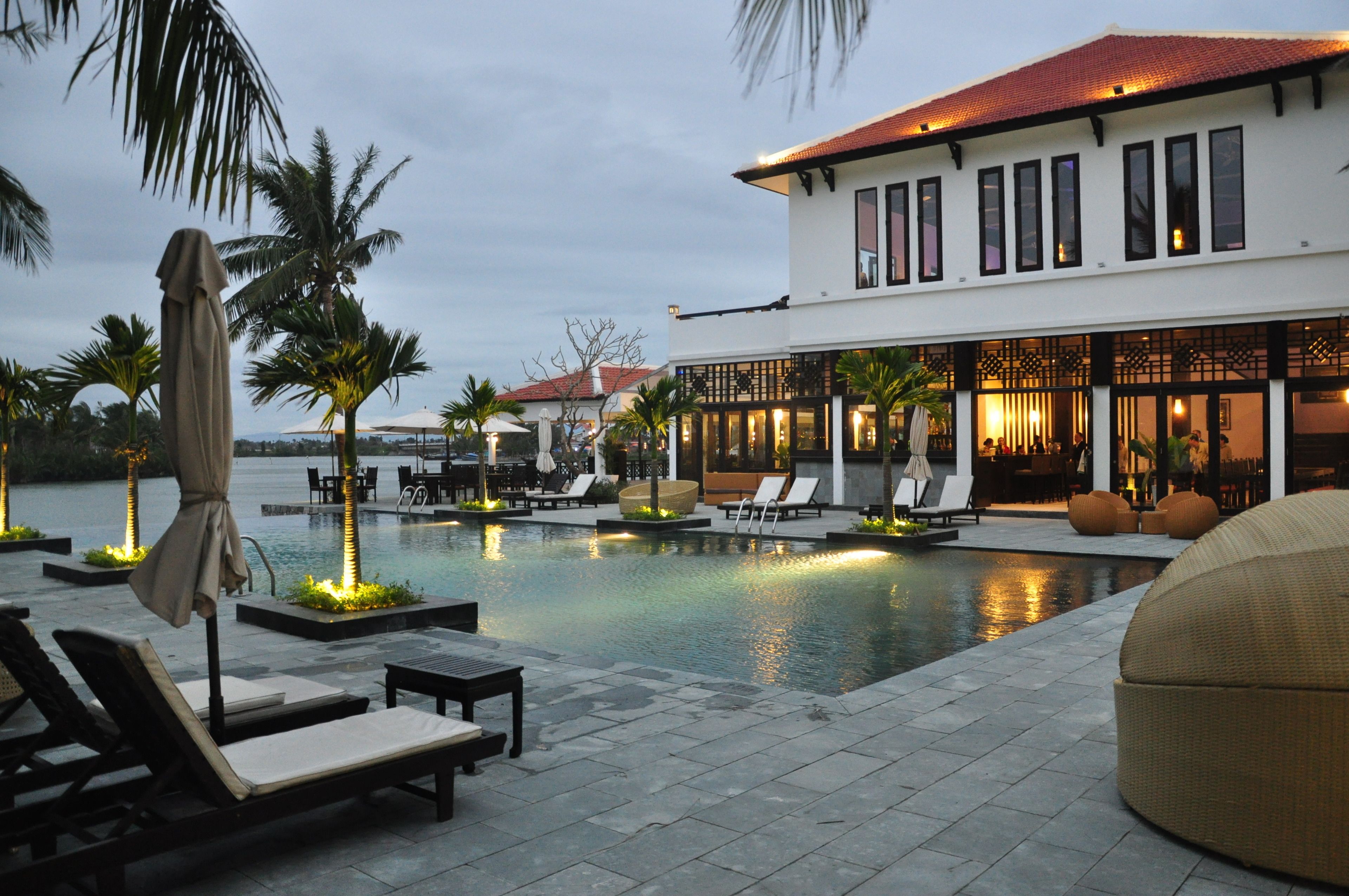 A resort with a swimming pool, lounge chairs, and a building with large windows.