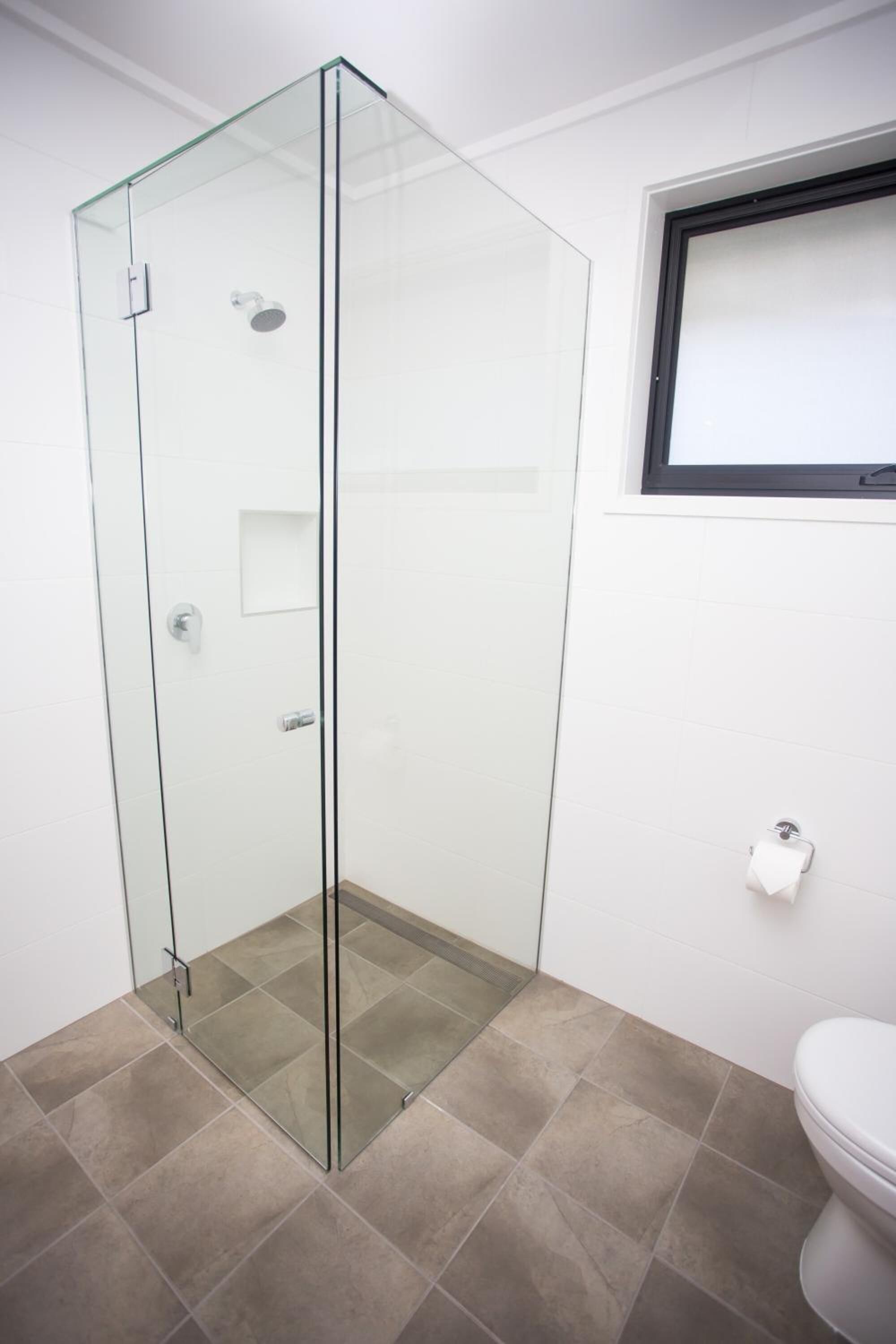 Un baño moderno con ducha envuelta en vidrio, inodoro y ventana sobre el lavabo.