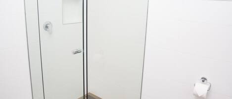 A modern bathroom with a glass-enclosed shower, a toilet, and a window above the sink.
