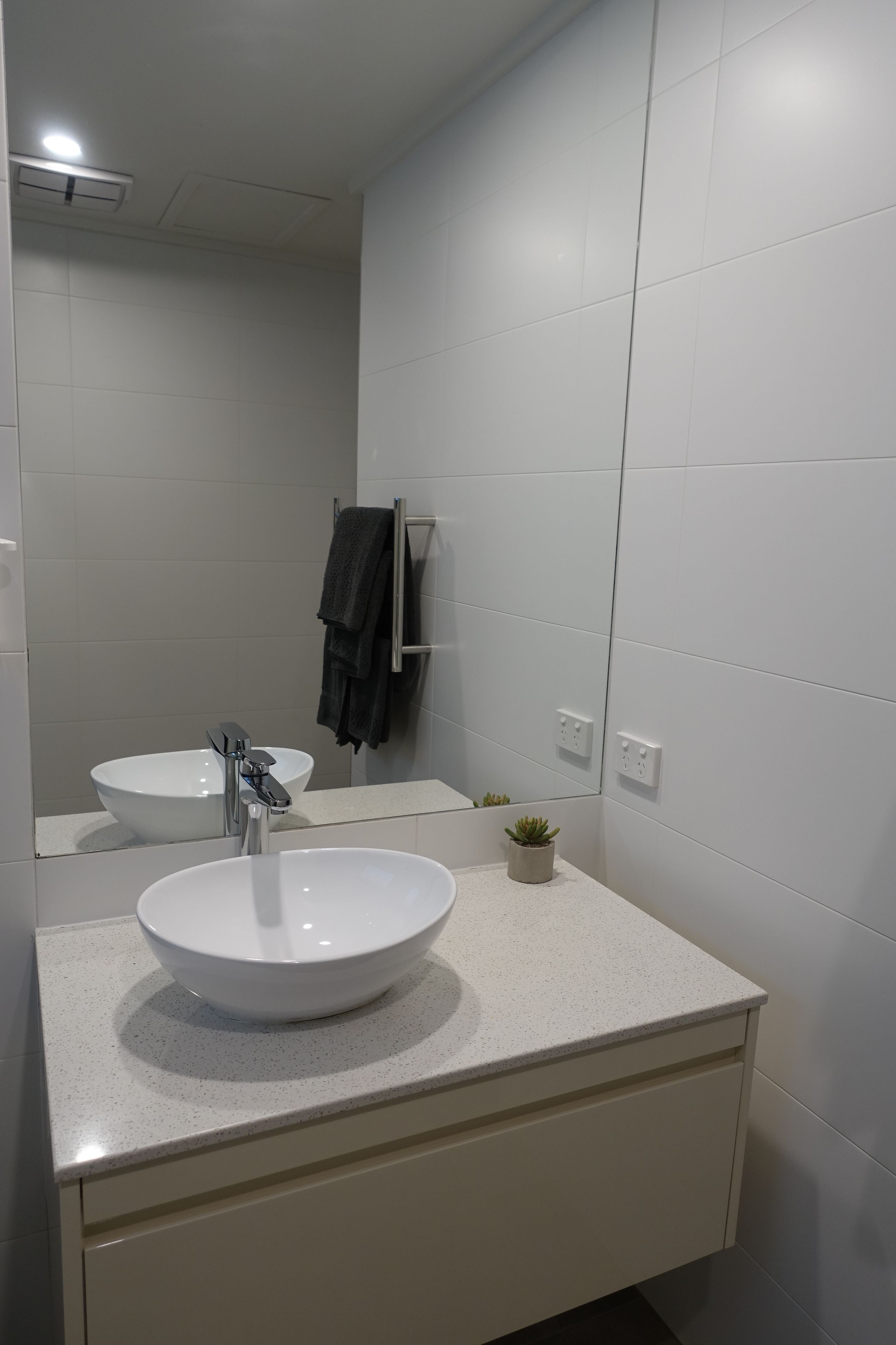 Une salle de bain moderne avec un lavabo blanc, un miroir et un porte-serviettes.