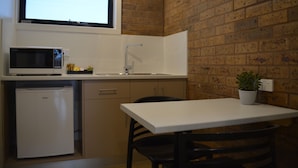 A compact kitchen with a microwave, refrigerator, sink, and a small table with a chair.