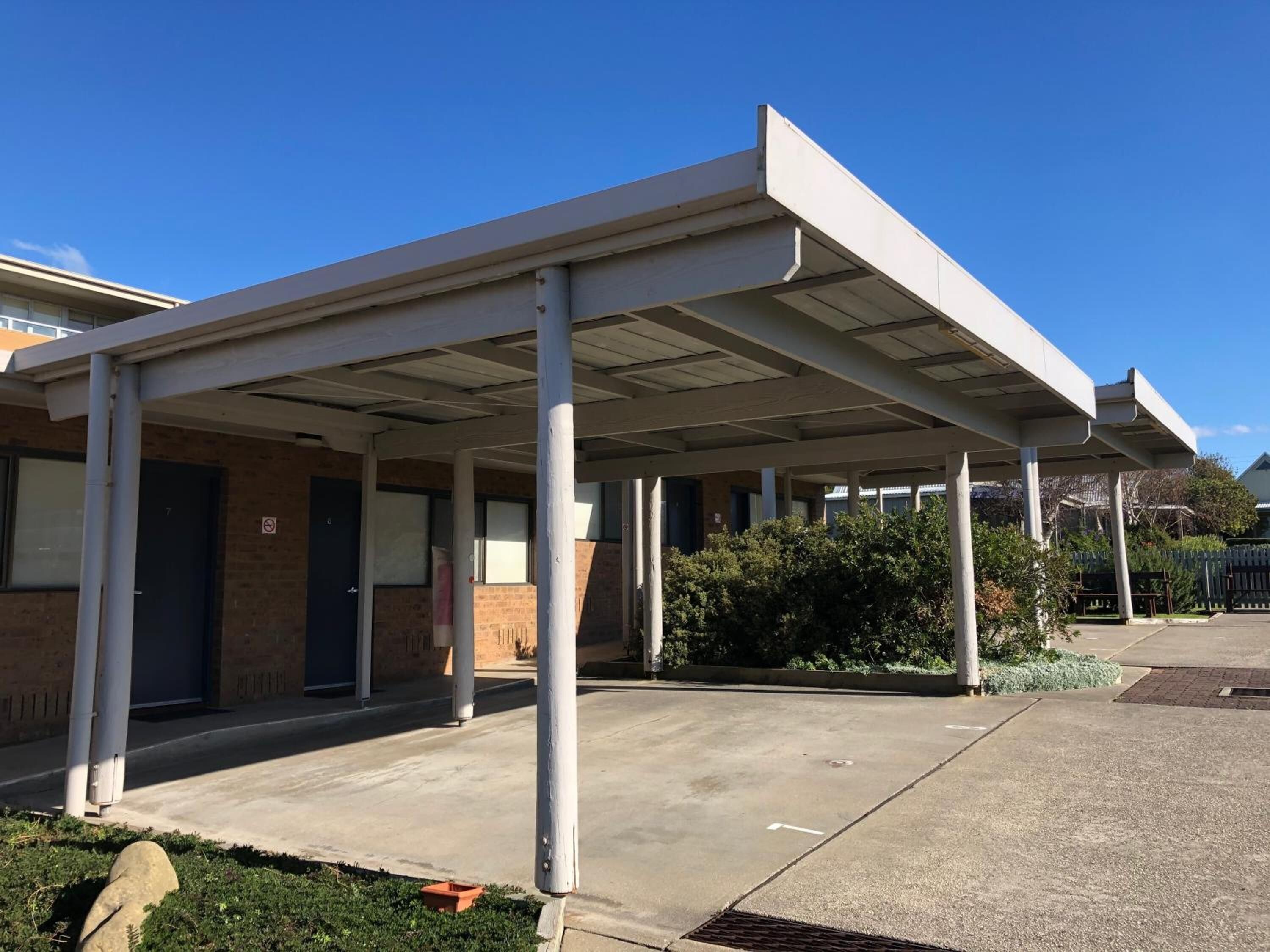 A covered outdoor area with a concrete floor, columns, and a building entrance with a door.