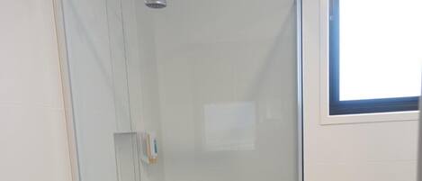 Un área de ducha con paredes de vidrio, un panel de control, una ventana y una puerta.